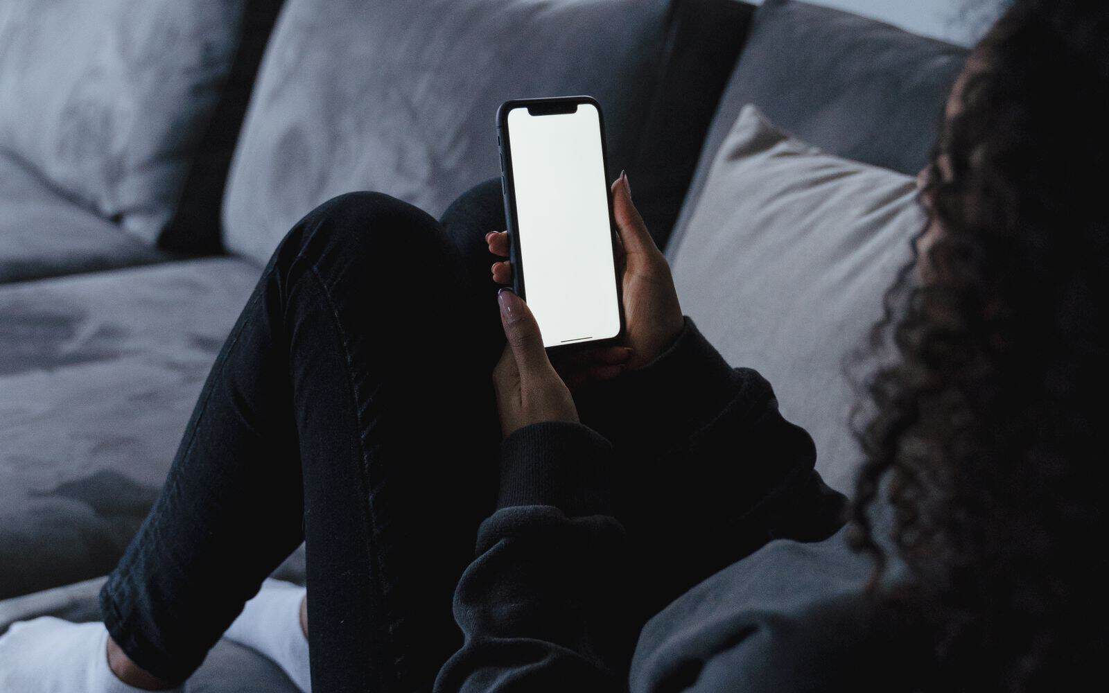 Person sjekker mobilen hjemme i sofaen