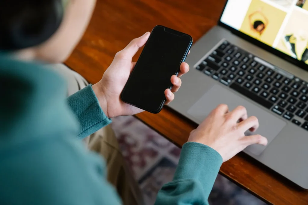 Person bruker mobil og laptop hjemme