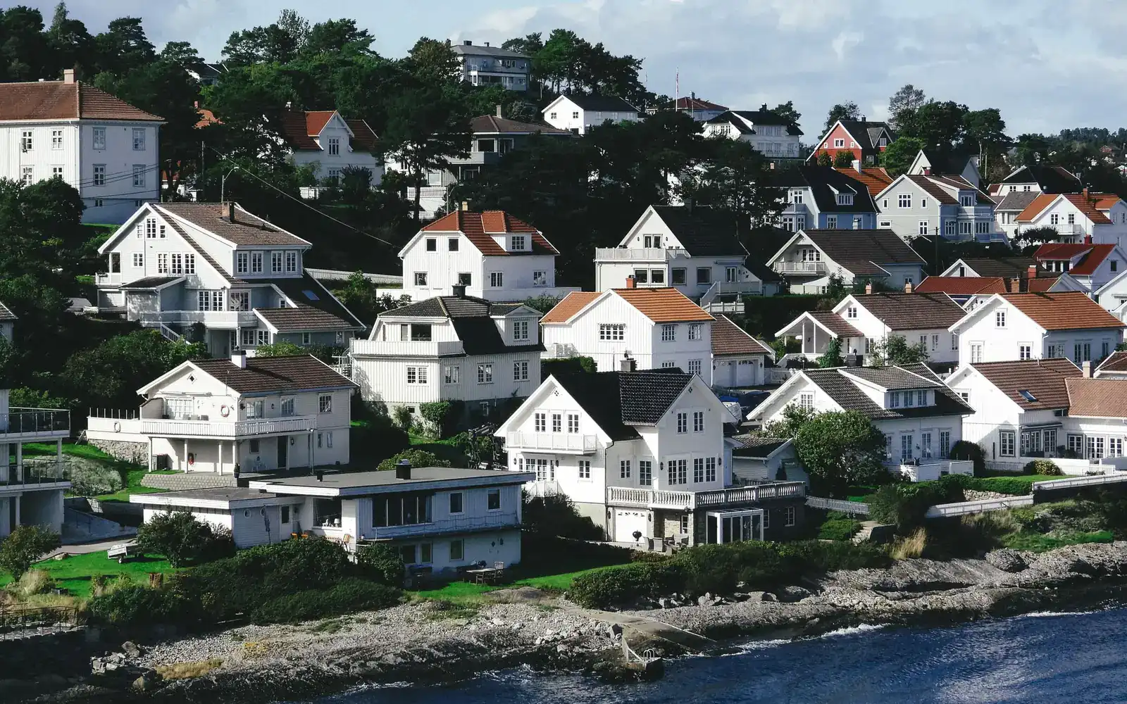 Hvite trehus på en høyde ved sjøen i en norsk kystby