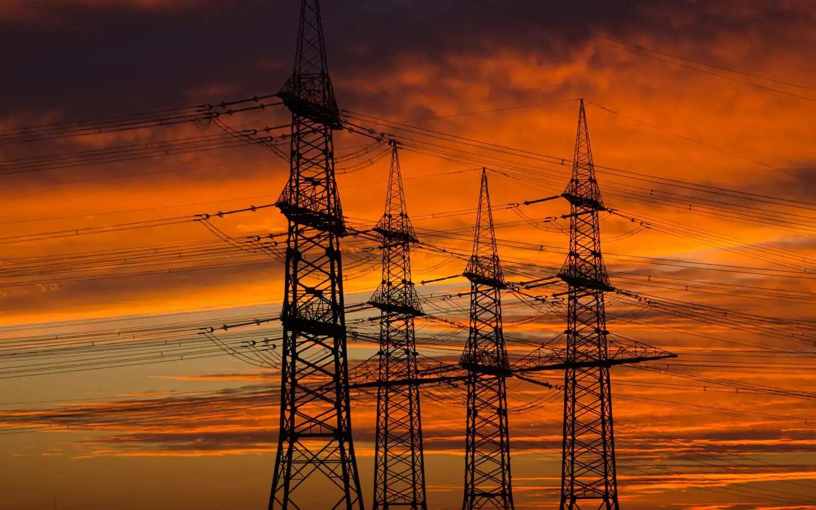 Silhuetter av høyspentmaster mot en oransje solnedgang