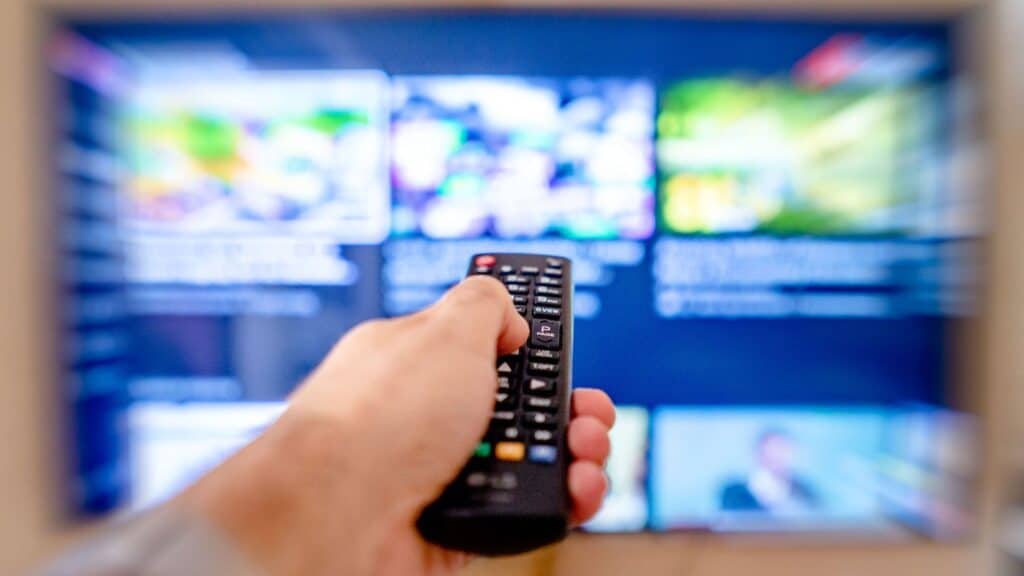 Hånd som holder en fjernkontroll mot en TV-skjerm med menyen til en strømmetjeneste