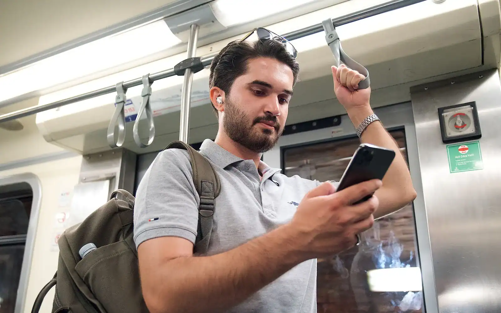 Ung mann med sekk bruker mobilen mens han står på T-banen
