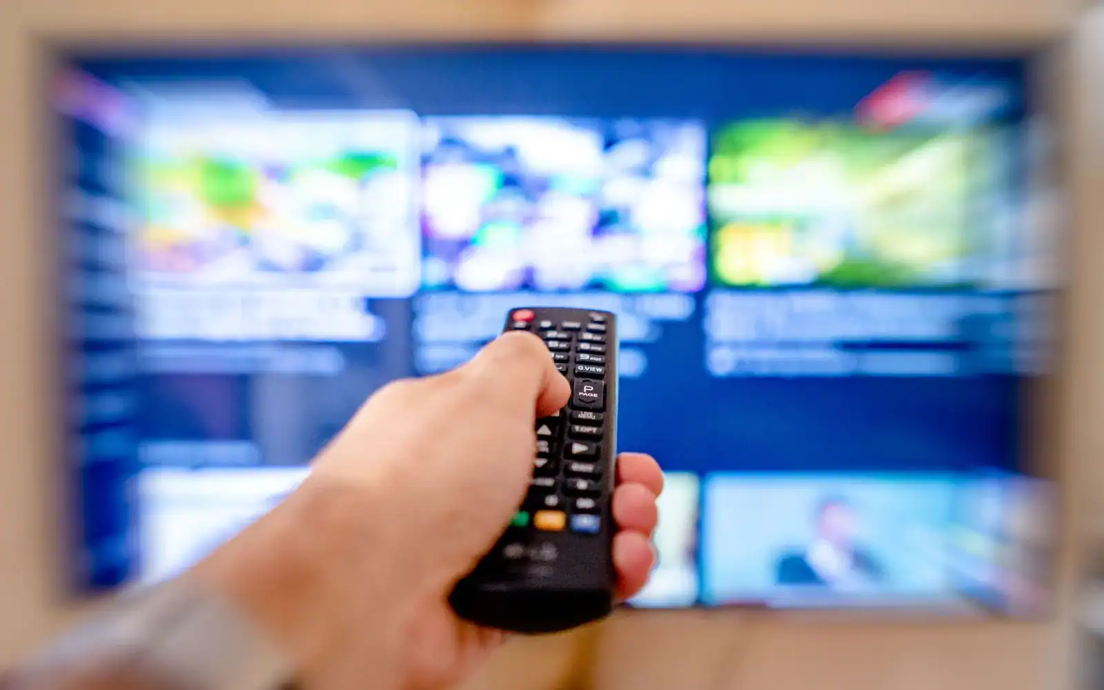 Hånd med fjernkontroll rettet mot en TV som viser et rutenett av apper