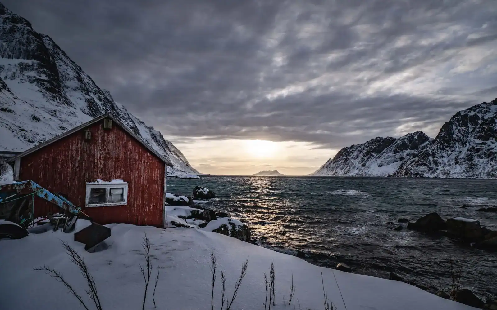 Rød hytte i snø ved fjorden i lavt vinterlys