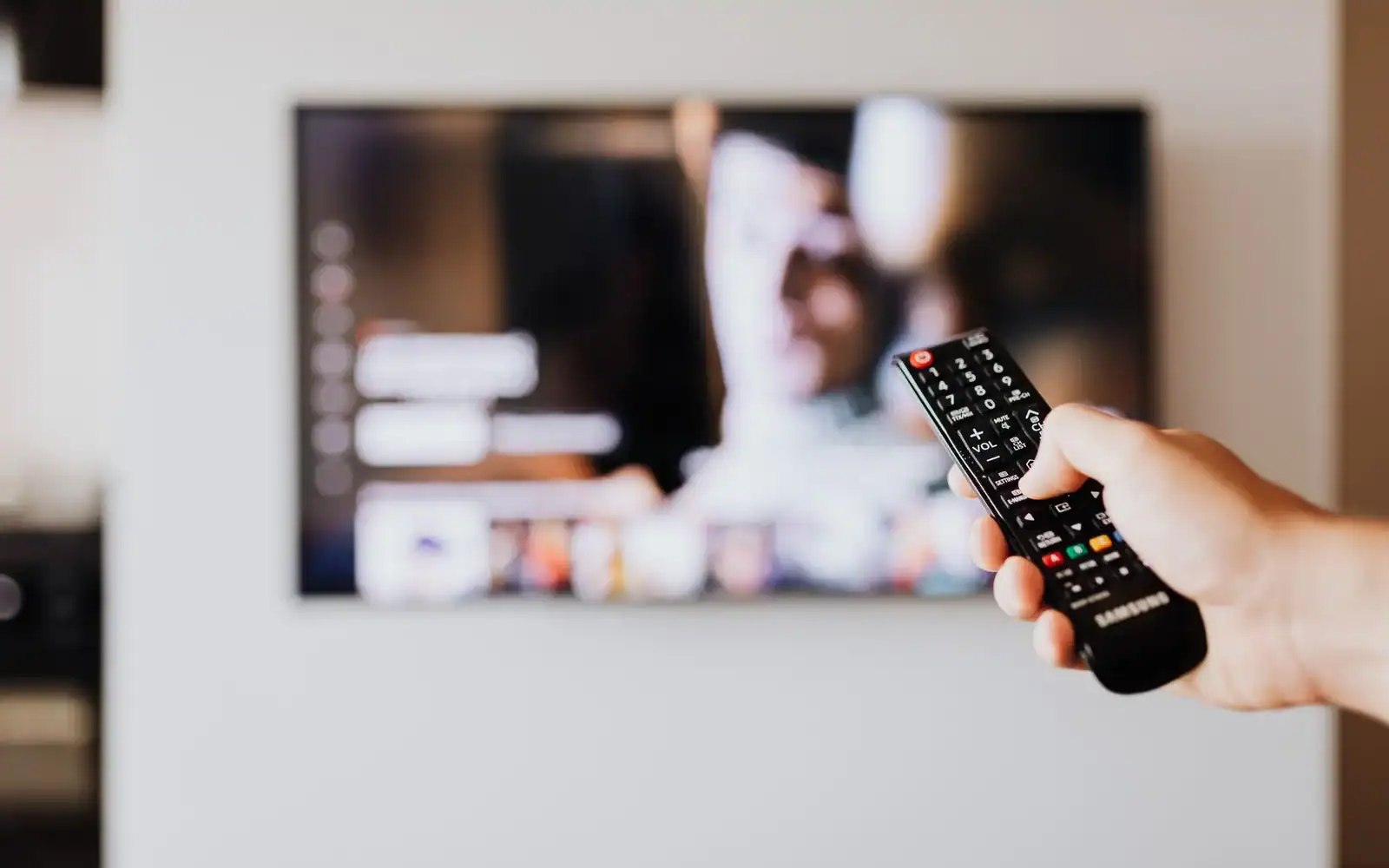 Hånd med fjernkontroll rettet mot en TV-skjerm i stuen