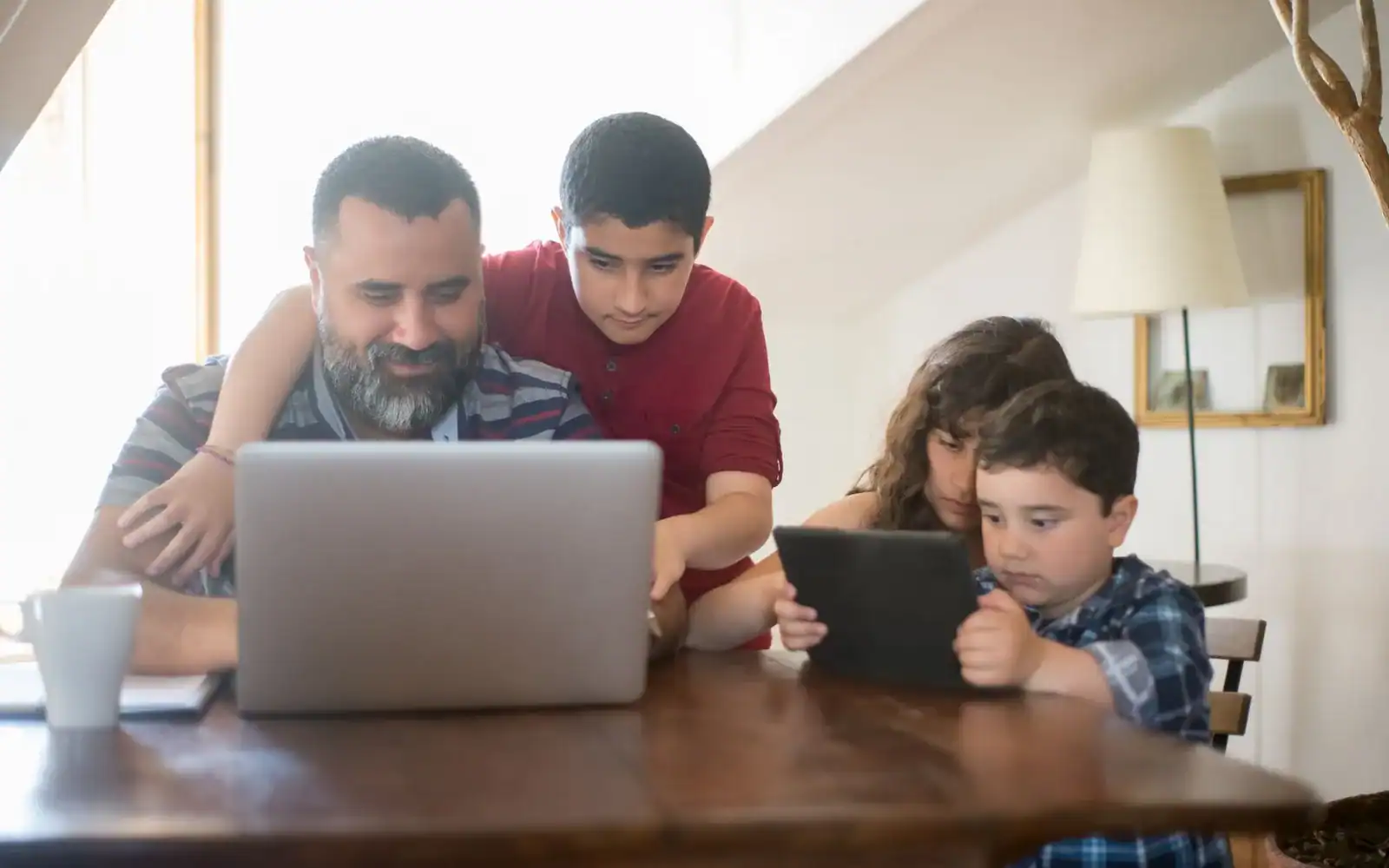 Far og tre barn samlet rundt en bærbar PC og et nettbrett