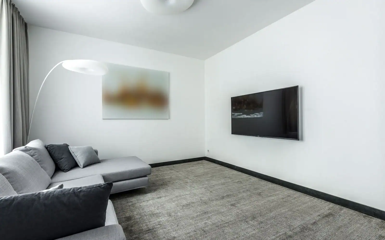 Lys stue med grå sofa og veggmontert TV