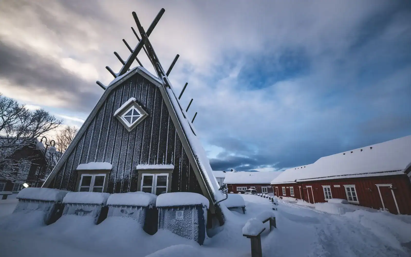 Snødekt trehus med spisst tak under en dramatisk vinterhimmel