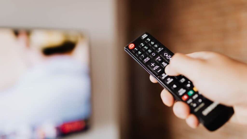 Hånd som peker en fjernkontroll mot en TV i en stue
